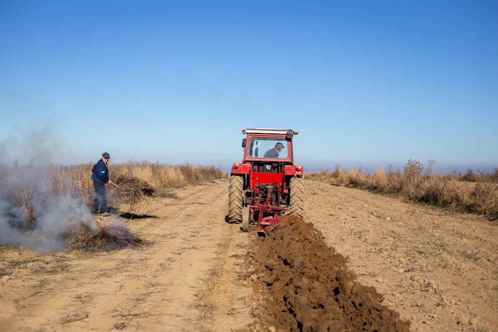 a man driving a tractor on a dirt road with a man standing next to it
