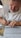 A person with a beard is sitting at a desk, focused on writing on a sheet of paper with a pen. The paper is filled with handwritten text. The person is wearing a white shirt and appears to be concentrating on the task. A ruler is placed on the paper.