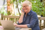 a woman on her phone while sitting at a table with a laptop