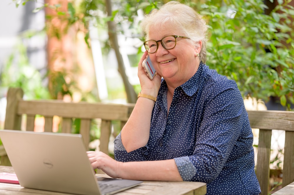 a woman on her phone while sitting at a table with a laptop