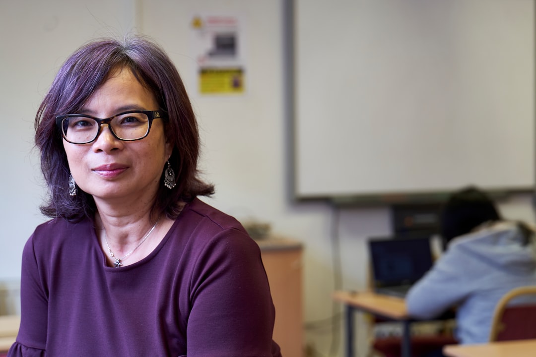 A woman at work in a classroom. She's sitting and staring at the camera.