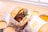 A gourmet burger is wrapped in paper labeled 'Savouri Eatery' and placed on a tray. The burger consists of a thick beef patty, lettuce, tomato, sauce, and melted cheese. Surrounding the burger are small metal cups filled with different dipping sauces.