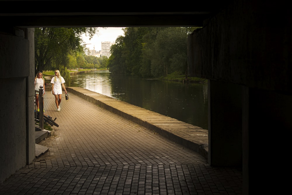 a couple of women walking down a brick path next to a river