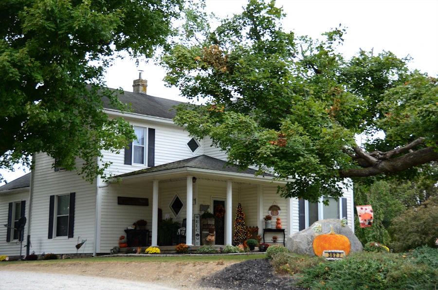 A white two-storey farmhouse with a front porch under big shade trees