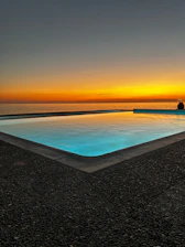 A serene swimming pool overlooking the sparkling sea at sunset.