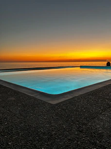 A serene swimming pool overlooking the sparkling sea at sunset.