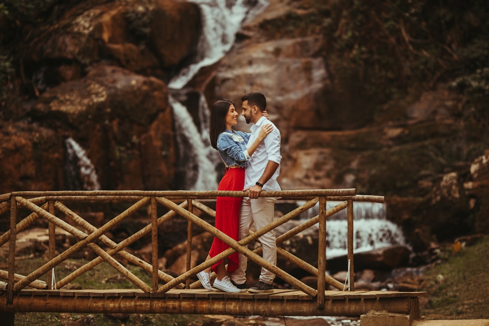 a man and woman kissing on a bridge over a waterfall