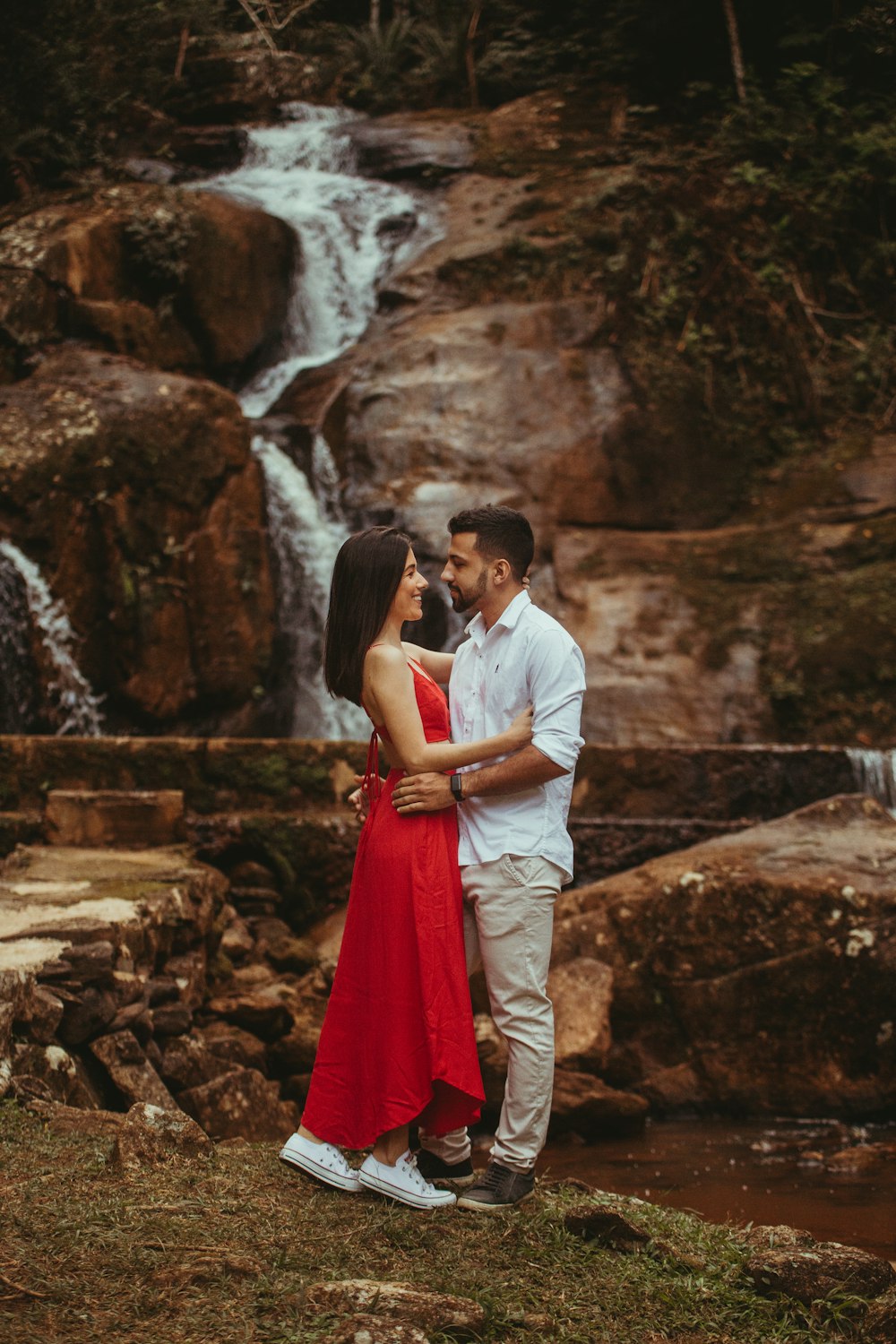a man and woman kissing in front of a waterfall