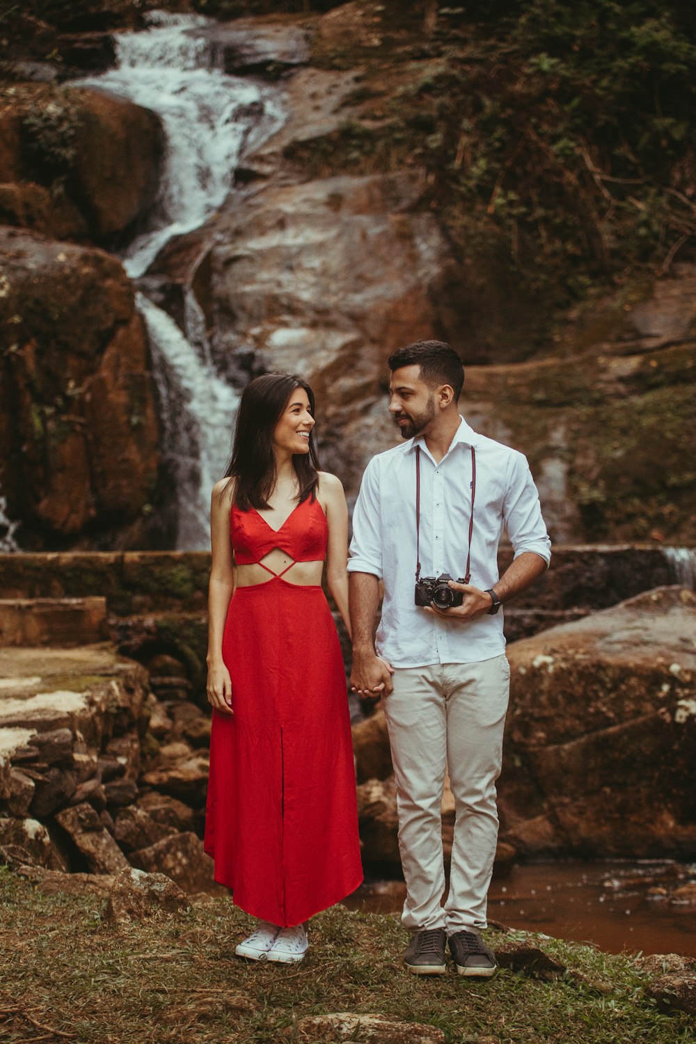 a man and woman posing for a picture in front of a waterfall