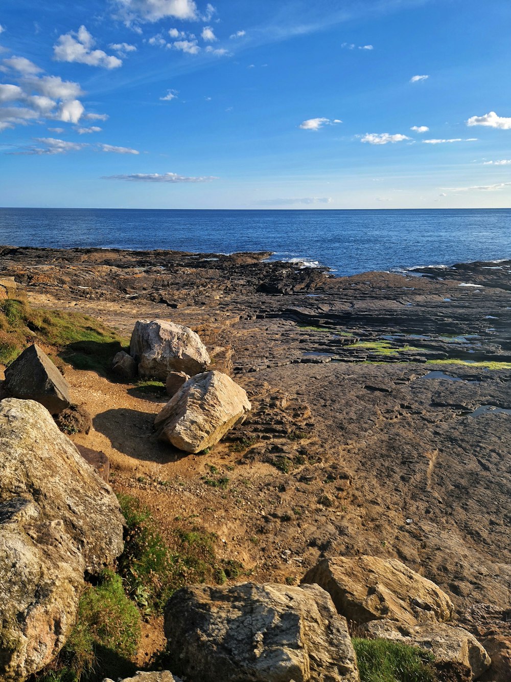 a rocky beach with blue sky and clouds