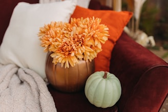 a vase with flowers, a pumpkin and burnt orange cushion