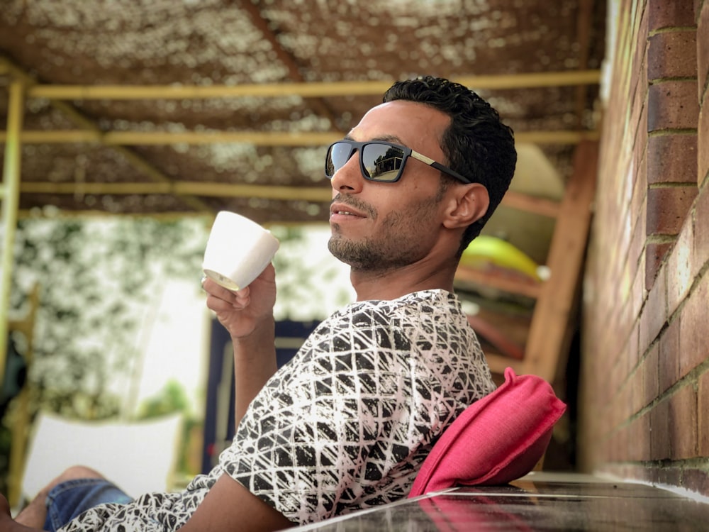 a man wearing sunglasses and holding a white cup