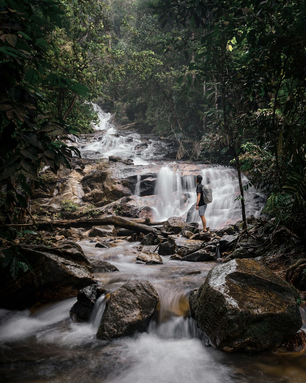 a couple people standing on rocks near a waterfall