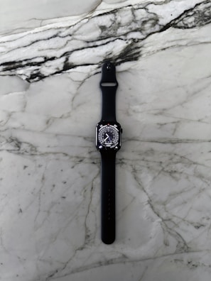 Close-up of a sleek black smartwatch with gold accents on a marble surface.