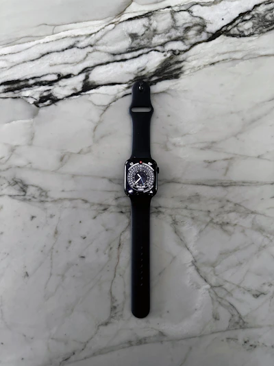 A sleek navy-blue smartwatch resting on a white marble surface with gold accents glowing softly.