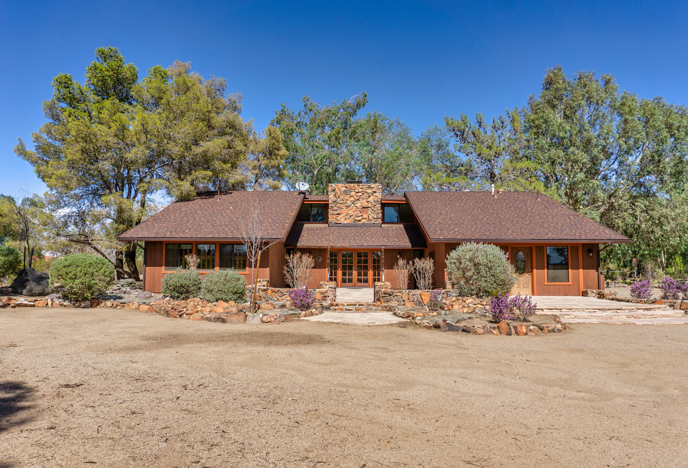 Sprawling single-story ranch house with stone chimney and mature trees
