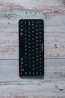 Portable foldable Bluetooth keyboard in use with a tablet on a wooden surface.