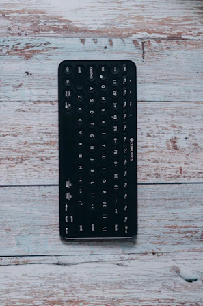 Portable foldable Bluetooth keyboard in use with a tablet on a wooden surface.