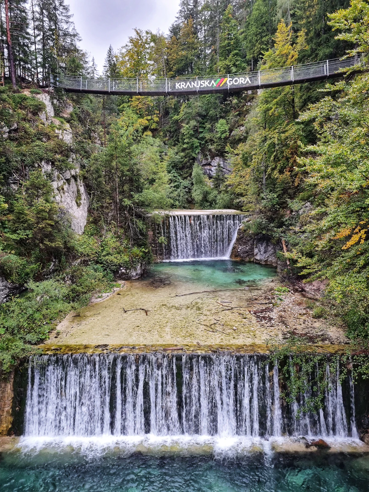 A footbridge marked Kranjska Gora over the Pišnica gorge, with small waterfalls below