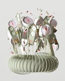 A collection of devices resembling clocks or gauges with colored indicators is attached to long, thin rods emerging from a coil structure. The devices have dials with red needles and various numerical scales. Surrounding the devices are individual pills and capsules floating through the air, giving a sense of motion.