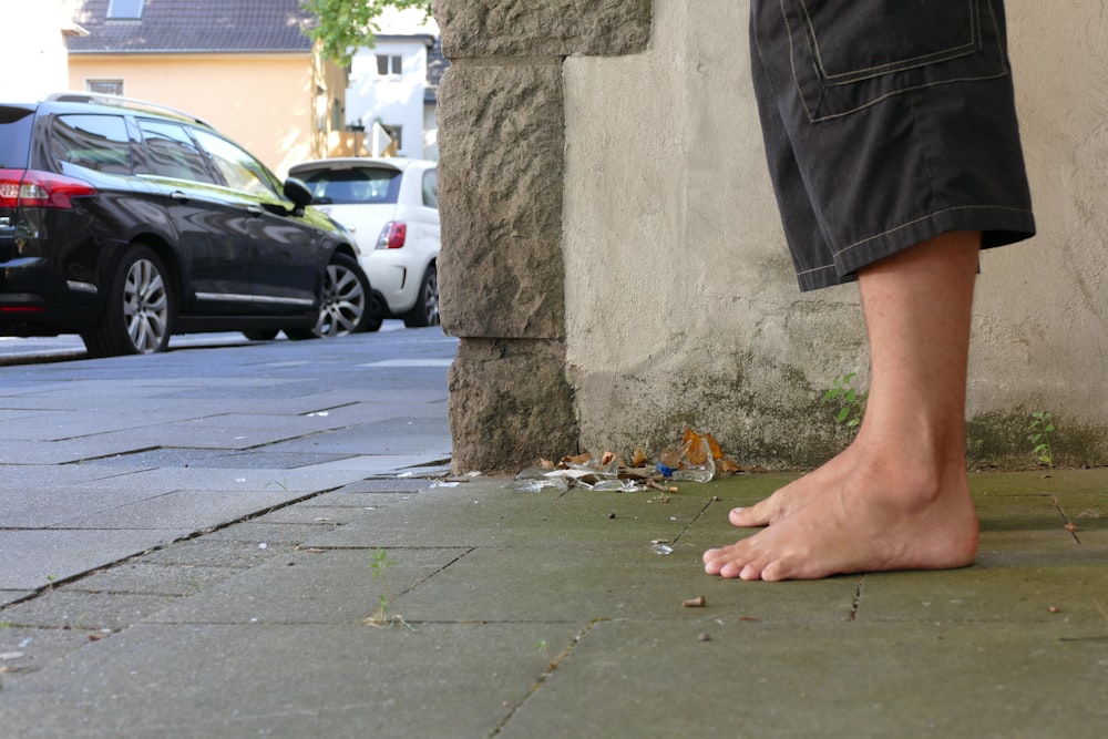 a person's legs and feet on a sidewalk by a tree