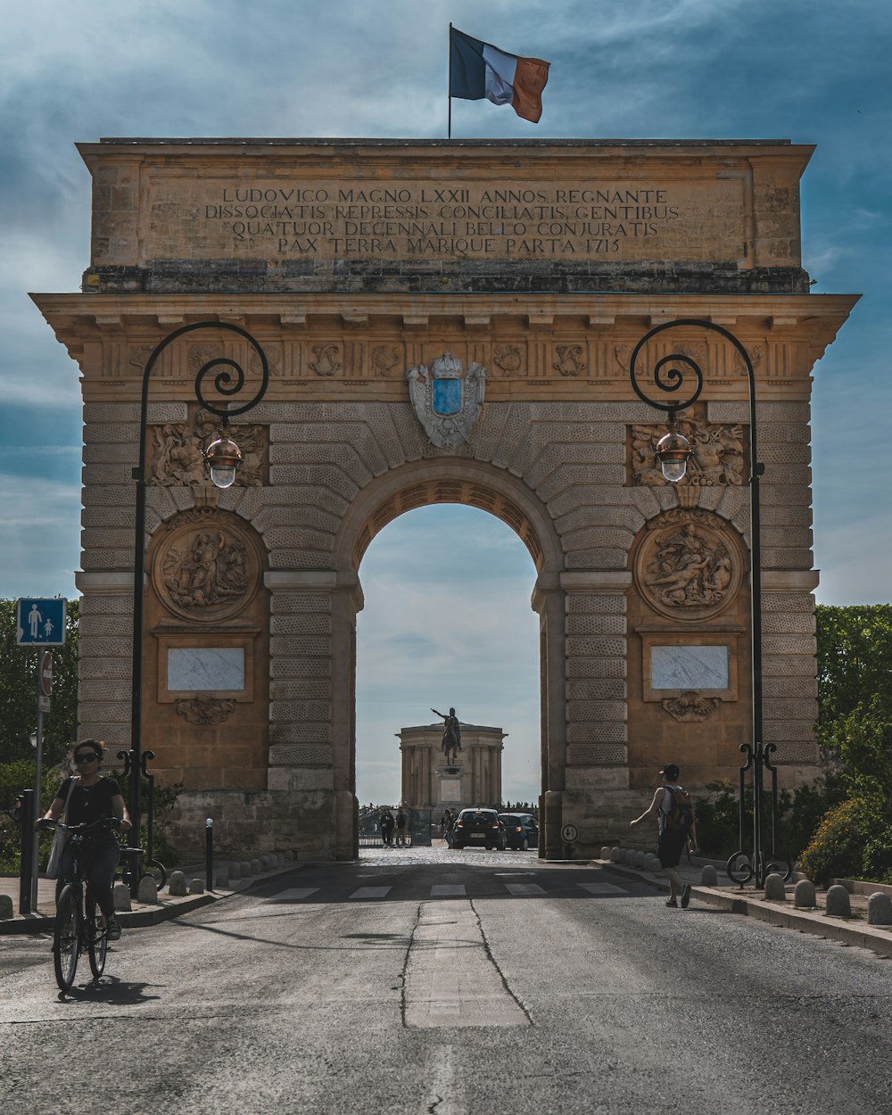 a large stone arch with flags with Porte du Peyrou in the background