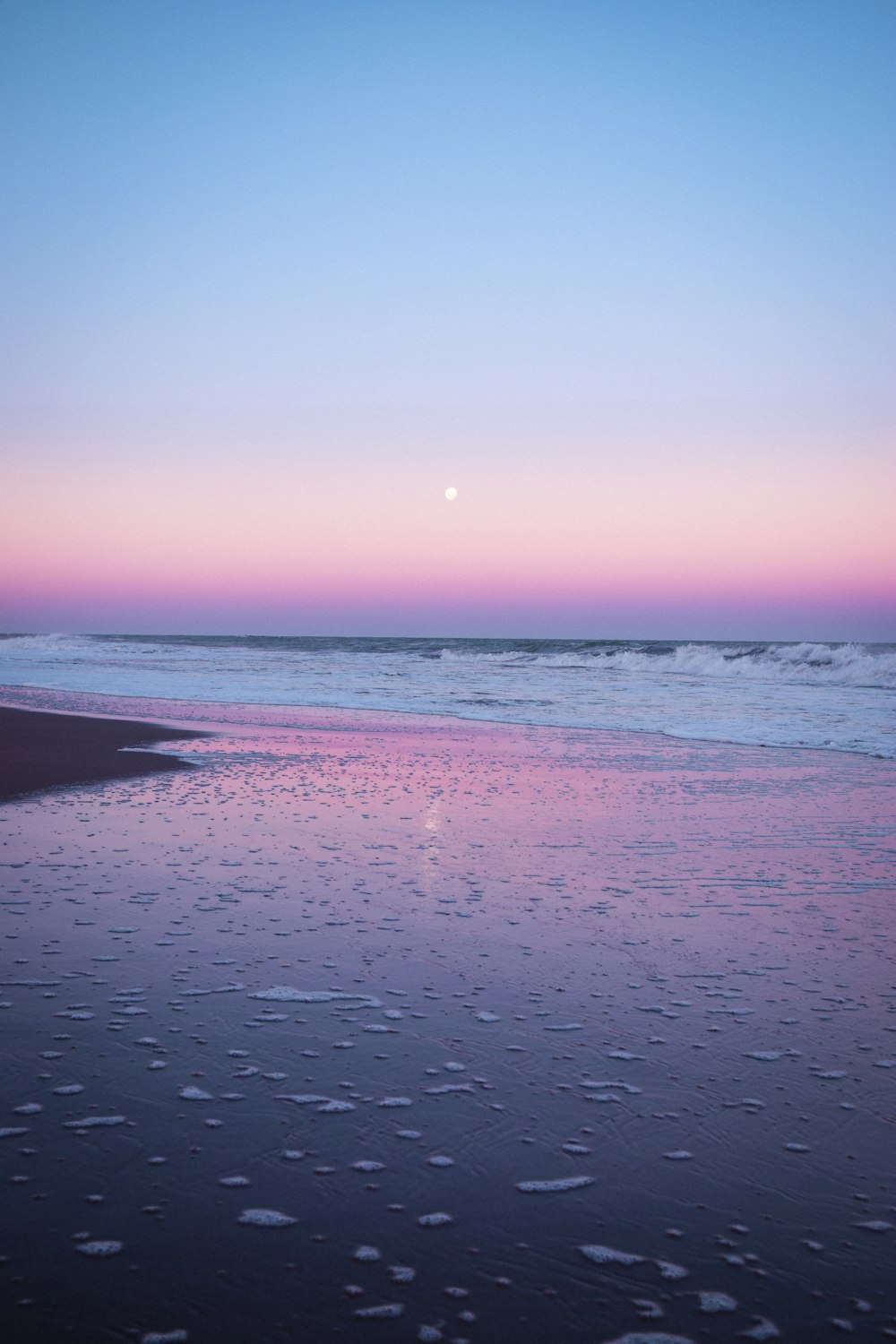 une plage avec un plan d’eau et un coucher de soleil