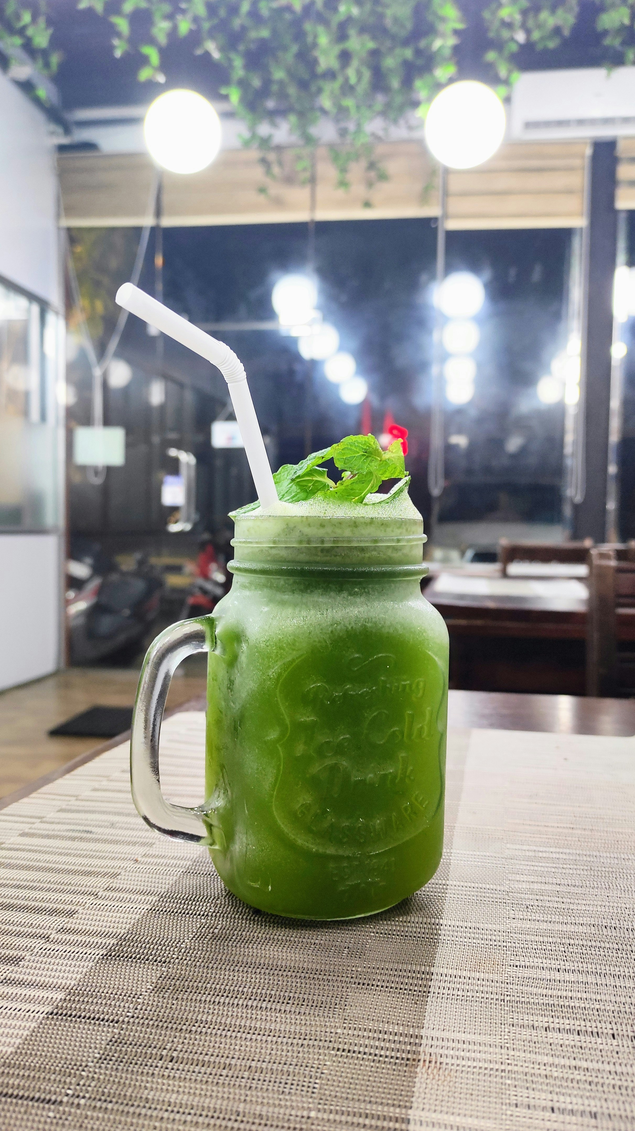 Vibrant green wheatgrass moringa spirulina energy shot glass surrounded by fresh green herbs and lemon bright white surface