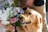 A golden retriever is sniffing a bouquet of flowers held by a person. The dog's mouth is slightly open, and its attention seems focused on the colorful flowers. The person holding the bouquet is wearing light-colored pants and is partially visible in the background.