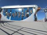 A modern building facade featuring bronze sculptures of people in traditional costumes, each posed dynamically against a backdrop of blue and white panels. The clear sky and architectural elements suggest an urban environment.
