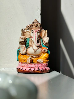 A peaceful Ganesh idol with a soft pastel finish, illuminated by natural sunlight.