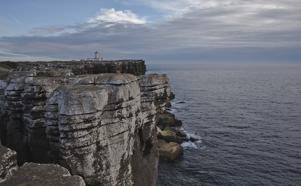 a rocky cliff with a lighthouse on it by the water