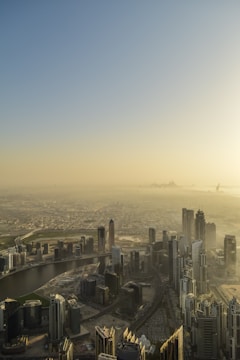 A sprawling urban cityscape featuring numerous modern skyscrapers stretching across the horizon under a hazy sky. The city is intersected by a winding river, and the buildings are densely packed, indicating a bustling metropolis.