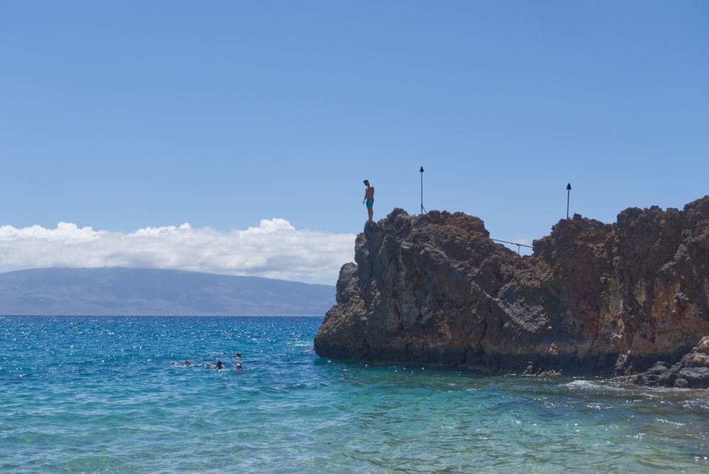 a group of people swimming in the ocean by a large rock
