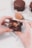 A close-up of hands holding a chocolate-covered snack with a creamy filling. The snack has been partially bitten, revealing its textured interior. In the background, there are other similar snacks and a dollop of peanut butter on a spoon.