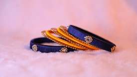 A set of intricately designed bangles featuring blue and orange bands adorned with small golden embellishments rests on a soft, fuzzy surface.