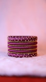 A stack of intricately designed purple bangles adorned with gold embellishments. The bangles are placed on a soft, fluffy surface, creating a luxurious and elegant ambiance.