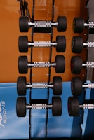 A set of modern gym equipment including dumbbells and resistance bands highlighted against a black backdrop with orange details.