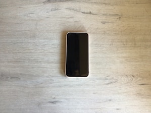 A sleek modern smartphone displayed on a wooden table with soft natural light.