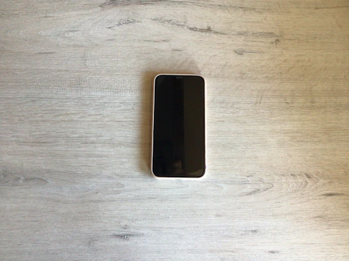 A sleek modern smartphone displayed on a wooden desk with soft natural lighting.