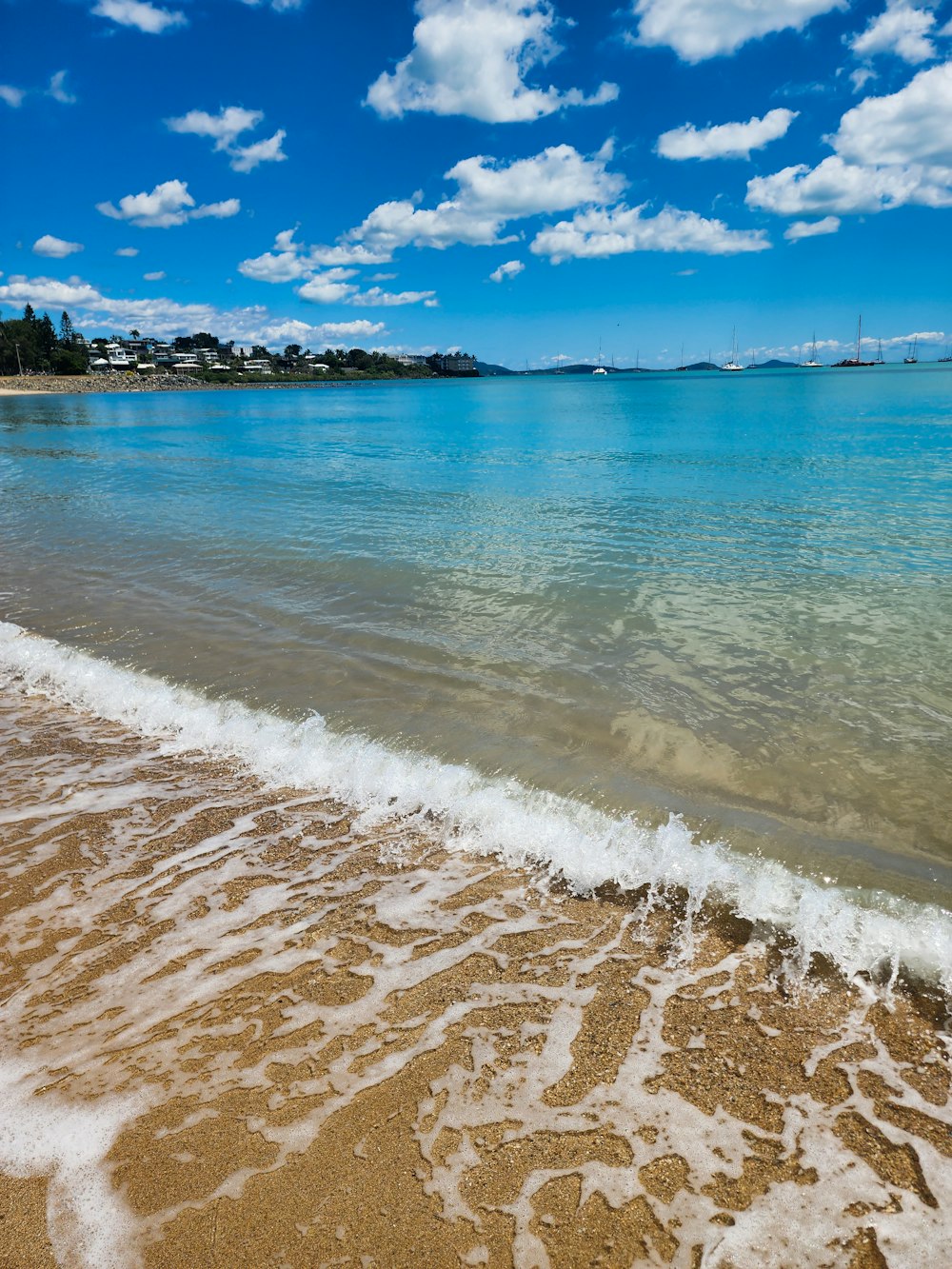 a sandy beach with blue water and a rocky island in the distance