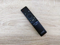 A sleek remote control resting on a wooden coffee table in front of a TV.