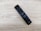A sleek black remote control is placed on a light wooden surface. The remote has several buttons, including a power button, directional buttons, and sound mode options. The surface has a textured, natural wood grain pattern.