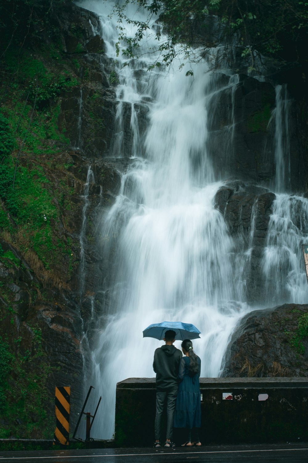 a couple standing under an umbrella in front of a waterfall
