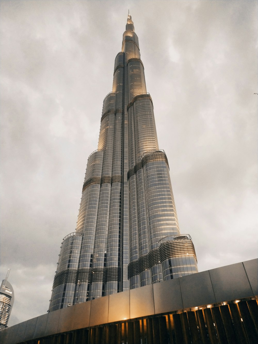 a tall building with a glass front with Burj Khalifa in the background