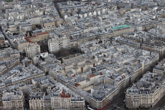 An aerial view of a densely packed urban area featuring a multitude of closely situated buildings and apartments. The architecture primarily consists of mid-rise structures with gray rooftops, aligned in a grid pattern, reflecting typical European urban design.
