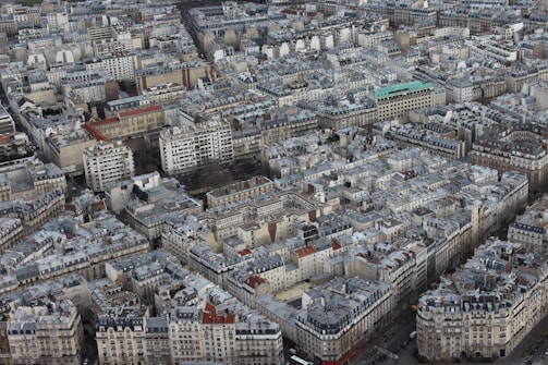 An aerial view of a densely packed urban area featuring a multitude of closely situated buildings and apartments. The architecture primarily consists of mid-rise structures with gray rooftops, aligned in a grid pattern, reflecting typical European urban design.