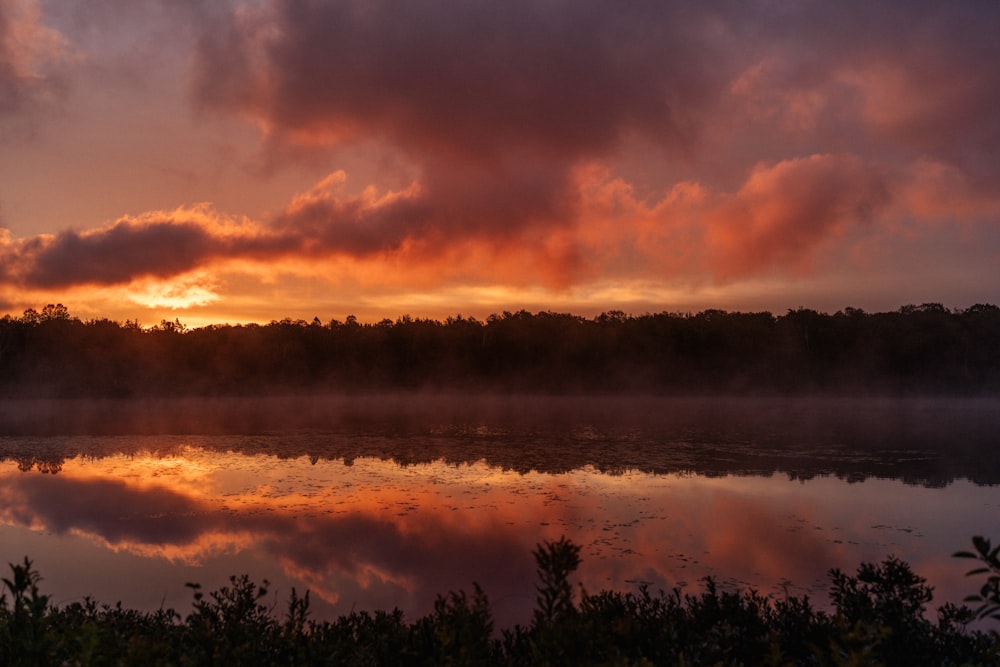 a body of water with trees and a sunset in the background