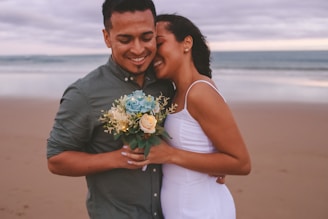 a man and woman holding flowers on a beach