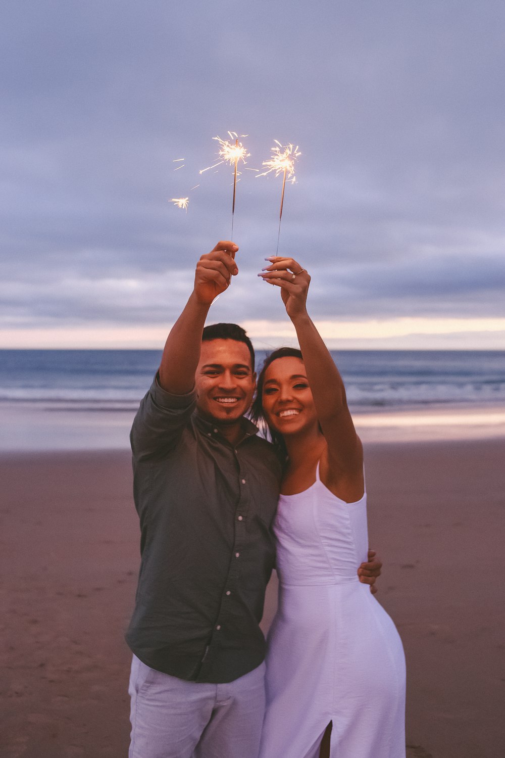 a man and a woman holding sparklers on a beach